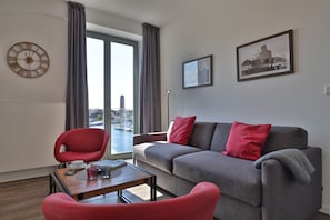 Una sala de estar moderna con un sofá gris, sillones rojos, una mesa de centro de madera y un gran reloj de pared.