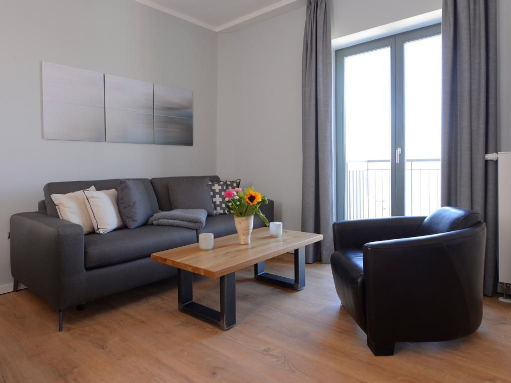 Ein modernes Wohnzimmer mit einem grauen Sofa, einem schwarzen Sessel und einem Holztisch mit Blumen in einer Vase.