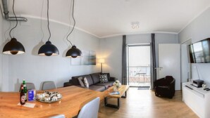 A modern living room with a sofa, coffee table, and a dining area with a wooden table and chairs. There is a TV on a stand and a balcony visible through the window. - Ohlerich storage app. 34 - Ohlerich Speicher App. 34 (Wismar)