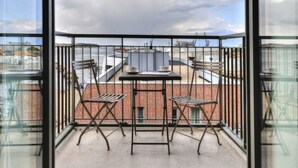 A balcony with two chairs and a table, overlooking a brick building and a cloudy sky. - Ohlerich storage app. 34 - Ohlerich Speicher App. 34 (Wismar)