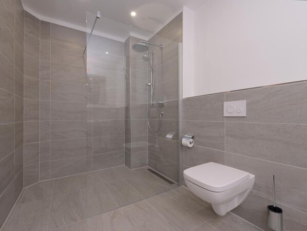 Ein modernes Badezimmer mit einer gläsernen Dusche, einer weißen Toilette und einem wandmontierten Spülhebel.