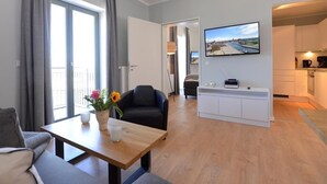 A modern living room with a sofa, a coffee table with flowers, a TV, and a kitchen area visible through an open door. - Ohlerich storage app. 34 - Ohlerich Speicher App. 34 (Wismar)
