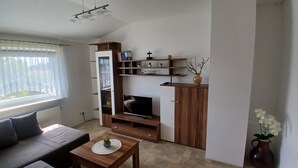 Ein Wohnzimmer mit einer Couch, einem Fernseher, Holzregalen und einem Fenster.