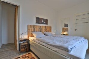 A bedroom with a wooden headboard, a single bed, a nightstand with a lamp, and a small rug.