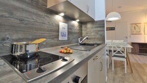 Ett modernt kök med en träpanel bakom arbetsbänken, rostfria köksmaskiner och en matplats med vita stolar.