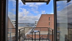 En balkong med ett bord och två stolar, med utsikt över en sjö eller ett annat vattendrag och byggnader.
