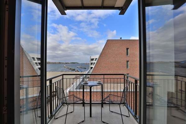 A balcony with a table and two chairs, overlooking a body of water and buildings.