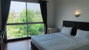 Une chambre d’hôtel dotée d’une grande fenêtre, d’un lit avec du linge de maison blanc, d’une table de chevet et d’un luminaire fixé au mur.