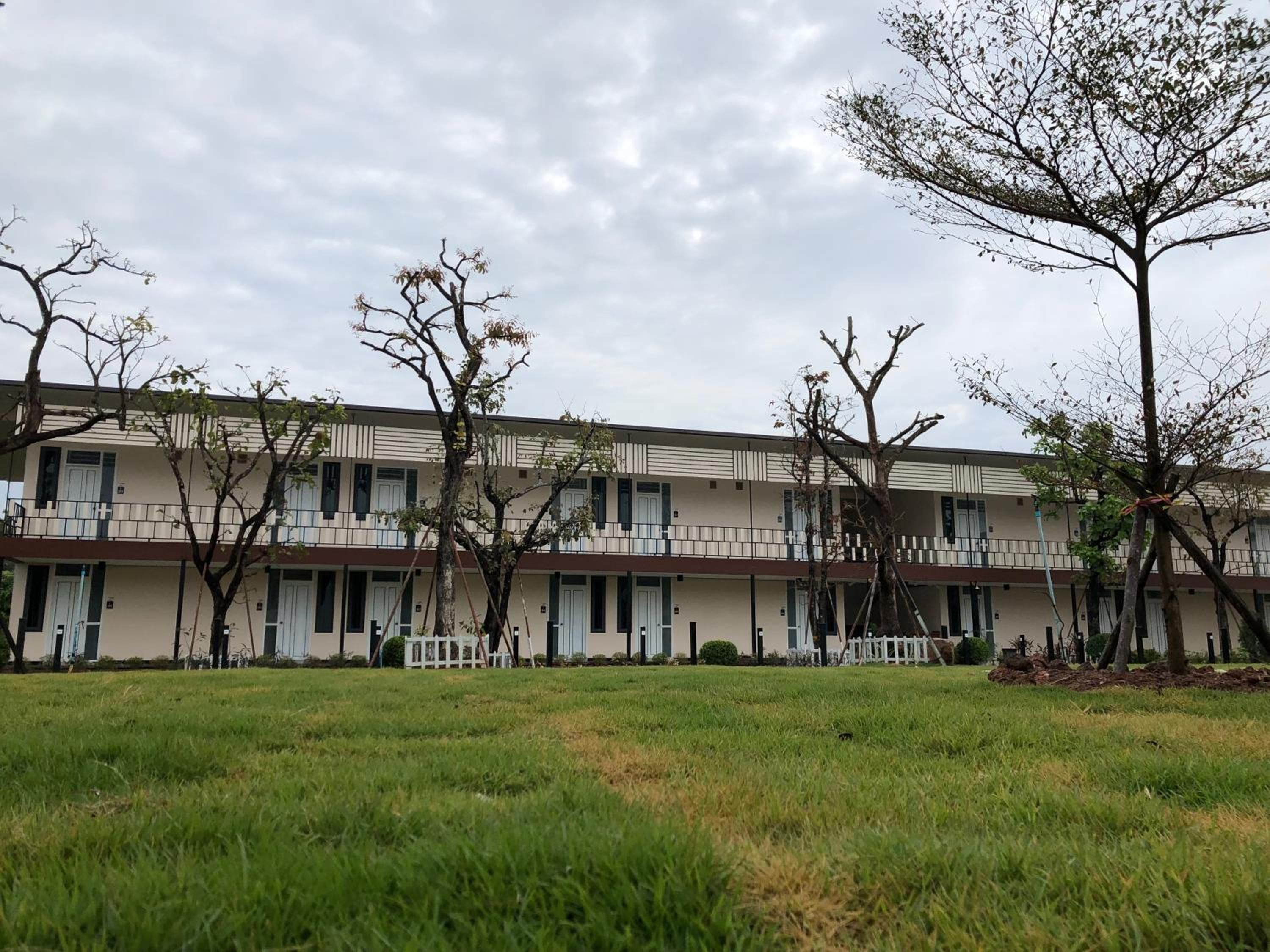 A multi-story building with a flat roof, a series of balconies, and a grassy courtyard.