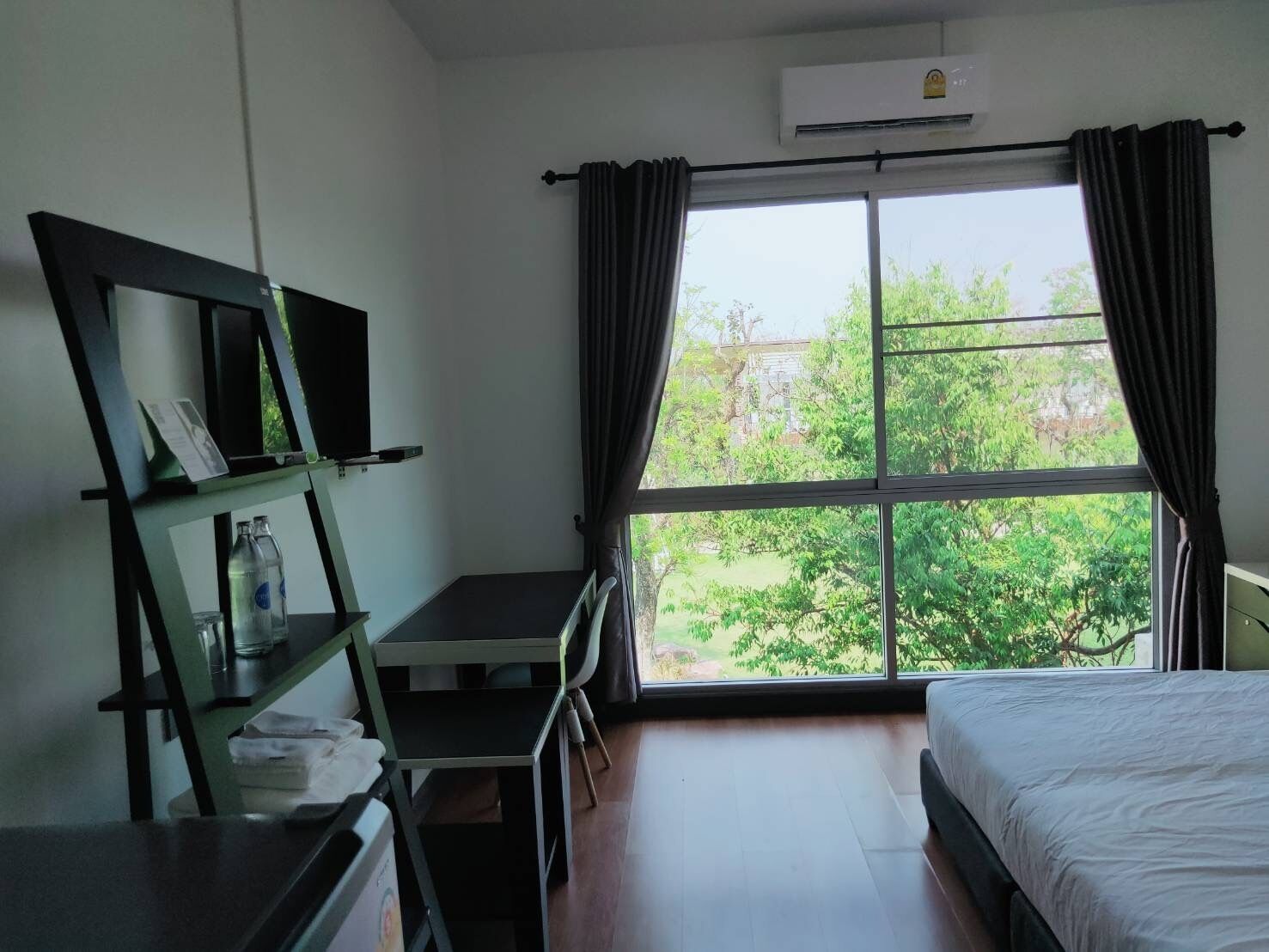 A hotel room with a bed, a desk, a chair, a TV, and a window with curtains.
