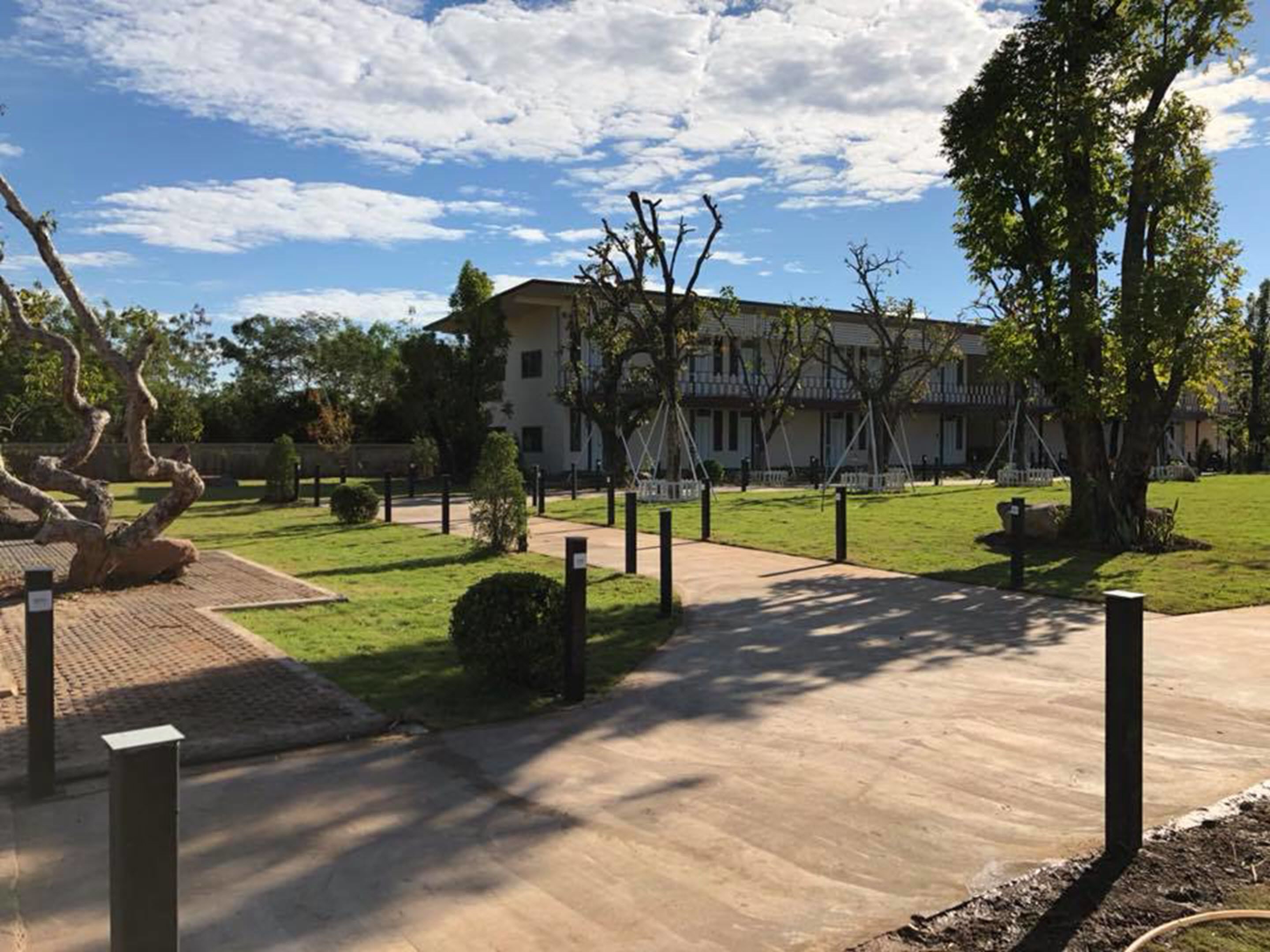Un edificio con un camino empedrado que conduce a una entrada con portones, rodeado de césped y árboles bien cuidados.