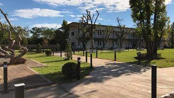 Un edificio con un camino empedrado que conduce a una entrada con portones, rodeado de césped y árboles bien cuidados.