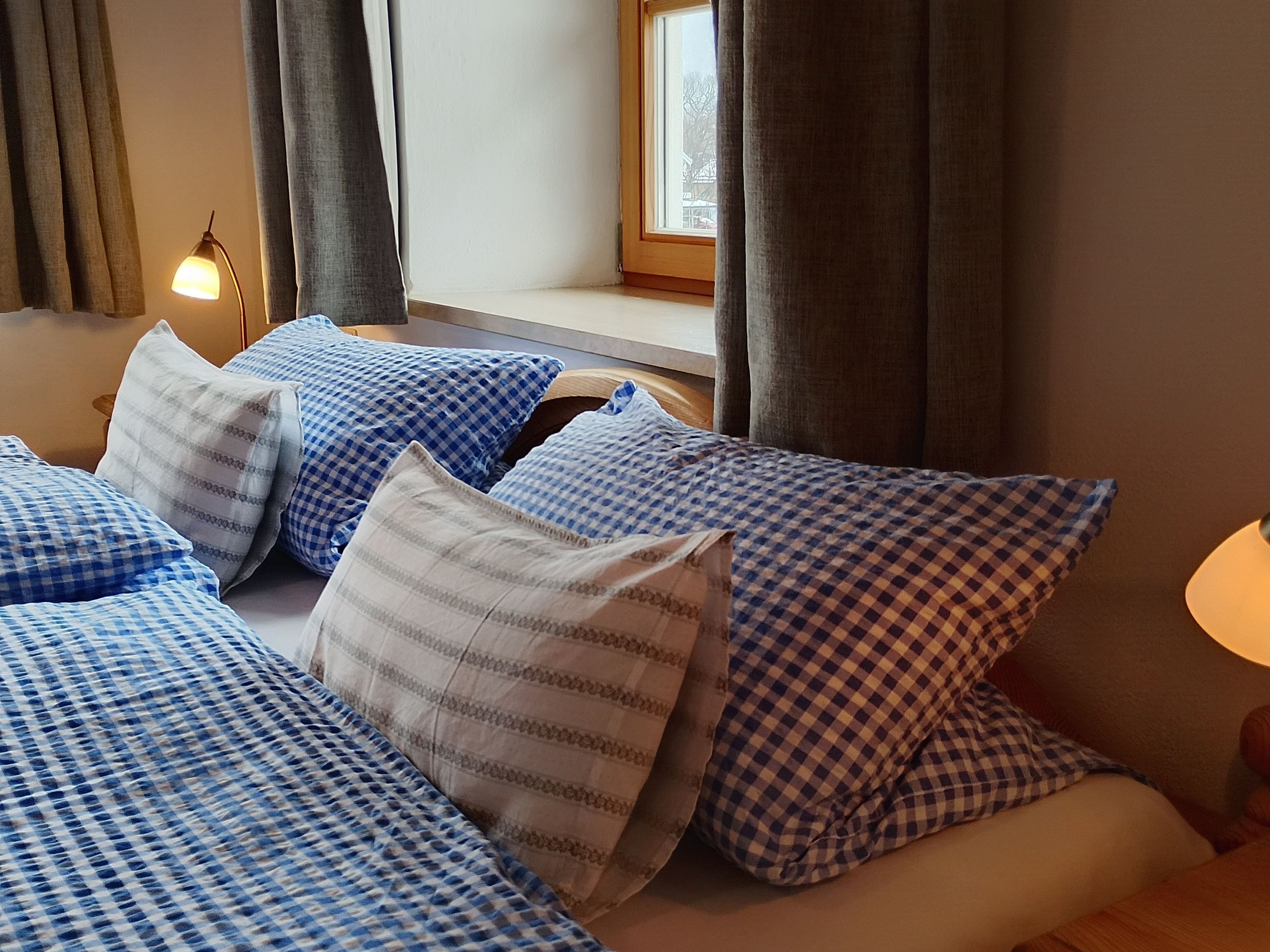Una habitación de hotel con cama, almohadas, lámpara y ventana.