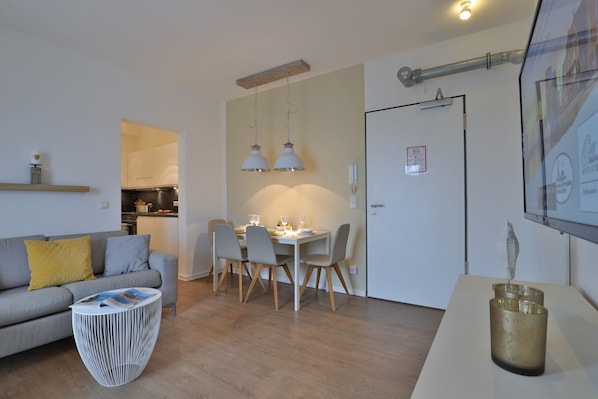 A modern living room with a sofa, dining table, and chairs, a kitchen in the background, and a hallway leading to a door. - Ohlerich storage app. 33 - Ohlerich Speicher App. 33 (Wismar)
