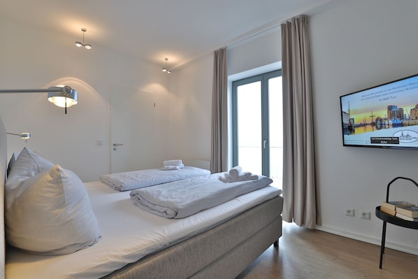 A modern hotel room with a bed, a desk, a television, and a view of the city.