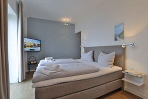Habitación de hotel moderna con una cama grande, un televisor de pantalla plana, una mesita de noche y vistas a la ciudad.