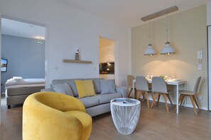 A modern living room with a sofa, a yellow armchair, a dining table with chairs, and a kitchen in the background.