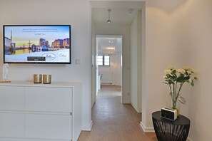 A hallway with a television displaying a welcome message, a white console table with decorative items, and a vase with flowers on a side table.