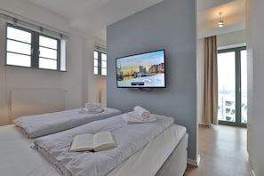 Une chambre d’hôtel avec deux lits, un téléviseur fixé au mur et une vue sur la ville par les fenêtres.