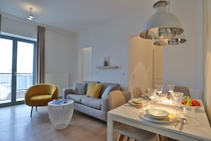 A modern living room with a sofa, a yellow armchair, a dining table set with glasses and a fruit bowl, and a large pendant light. - Ohlerich storage app. 33 - Ohlerich Speicher App. 33 (Wismar)