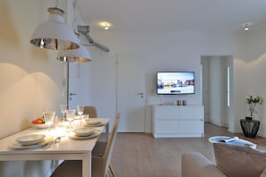 A modern living room with a dining area, a flat-screen TV mounted on the wall, and a white cabinet. - Ohlerich storage app. 33 - Ohlerich Speicher App. 33 (Wismar)