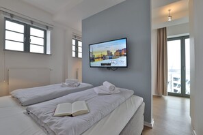 Ein Hotelzimmer mit zwei Betten, einem an der Wand befestigten Fernseher und Blick auf die Stadt durch die Fenster.