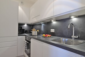 A modern kitchen with white cabinets, a stainless steel sink, and a black countertop.