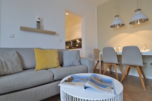 A modern living room with a grey sofa, a yellow pillow, a white coffee table with a magazine, and a dining area with a table and chairs. - Ohlerich storage app. 33 - Ohlerich Speicher App. 33 (Wismar)