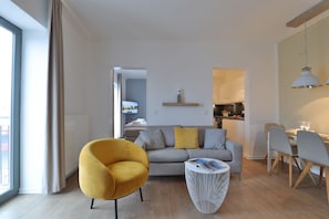 Ein modernes Wohnzimmer mit einer Couch, einem gelben Sessel, einem weißen Couchtisch und einem Essbereich mit Tisch und Stühlen.