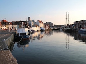 Ein ruhiger Hafen mit vertäuten Booten, Gebäuden am Wasser und wolkenlosem Himmel.