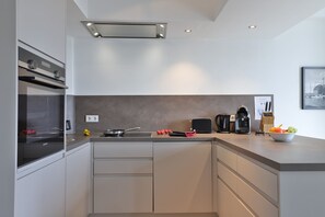 A modern kitchen with a built-in oven, a coffee maker, and a bowl of fruit on the counter.