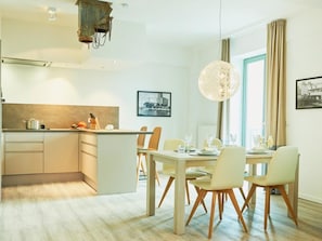 A modern kitchen with a central island, dining area with chairs, and a large pendant light.