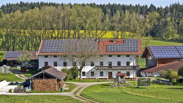 Ein ländliches Haus mit Solaranlage, einem Stall und einem grünen Feld.
