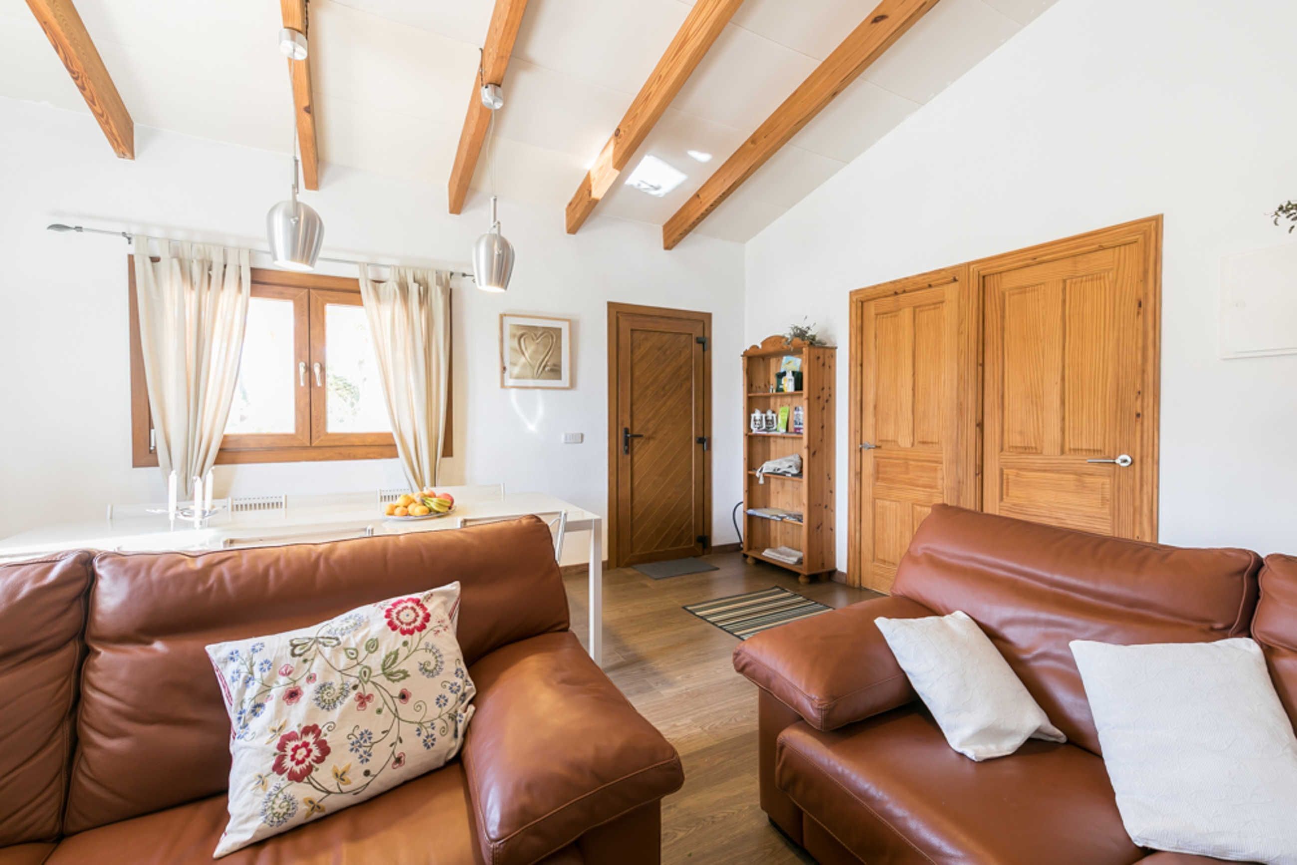 A living room with brown leather sofas, a white table, wooden beams on the ceiling, and a wooden door.