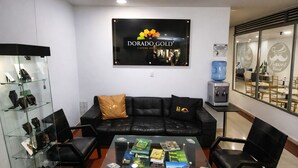 A modern interior with a black leather sofa, a glass coffee table with books, a glass display case with bags, and a sign for 'DORADO GOLD CADENA HOTEL'. - Hotel Dorado Gold Bogota (Bogotá)