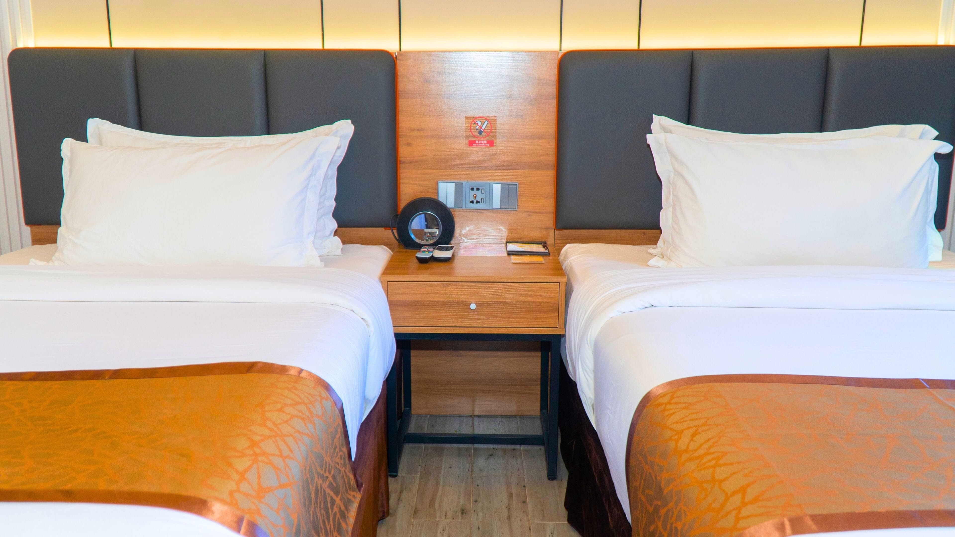 A hotel room with two beds, a wooden headboard, a nightstand with a clock, and a small table.