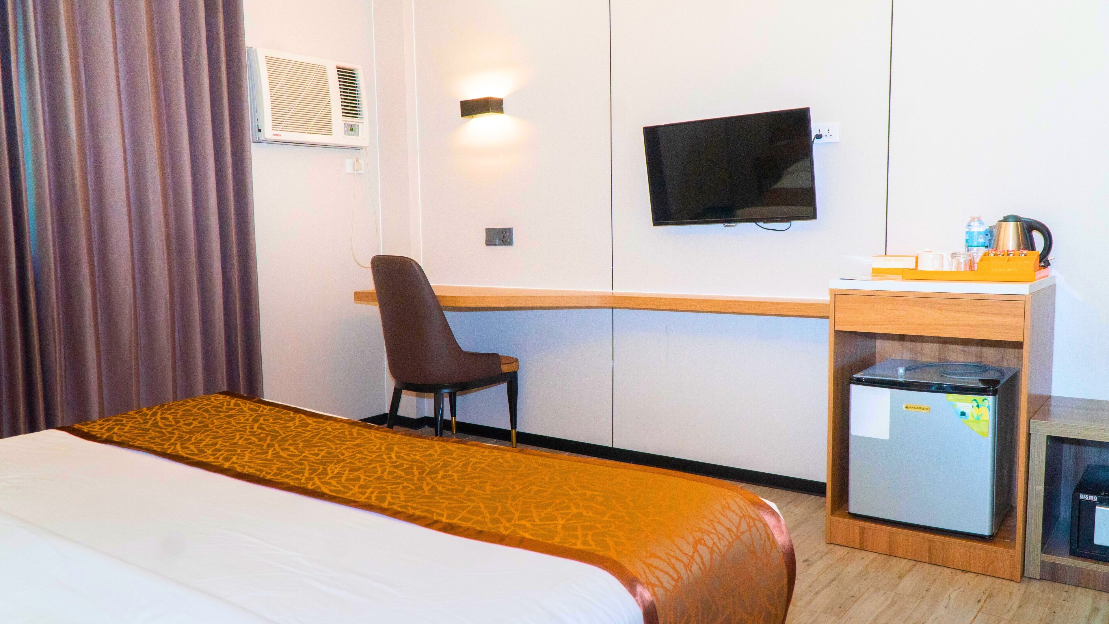 A hotel room with a bed, a desk, a chair, a television, and a minibar.