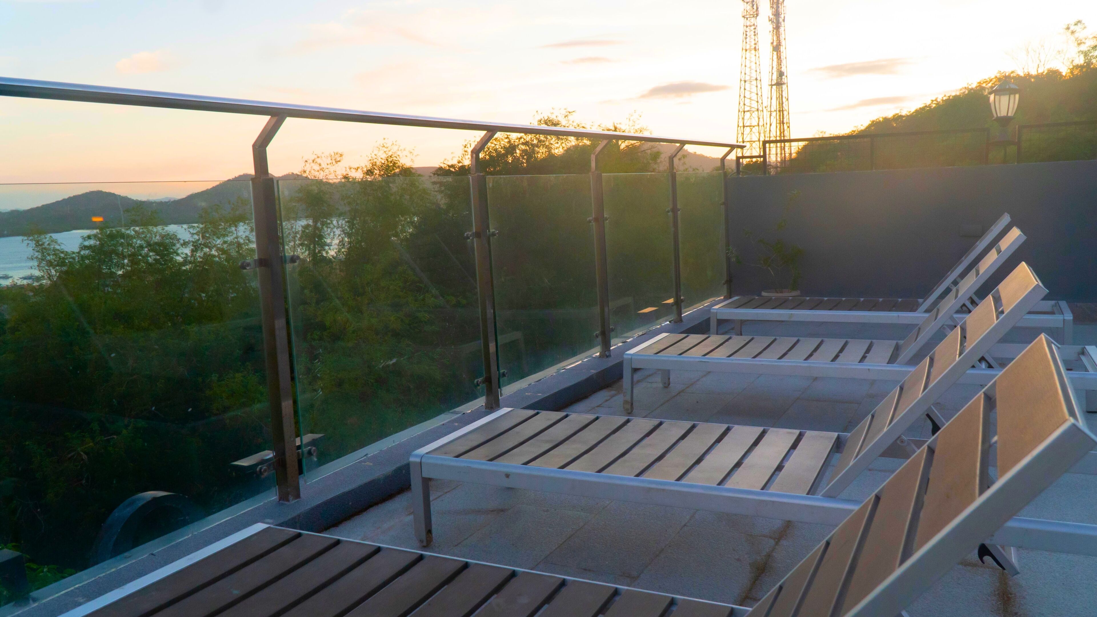 Un balcon doté de rampes en métal et de bancs en bois, offrant une vue sur une étendue d’eau et sur la verdure.