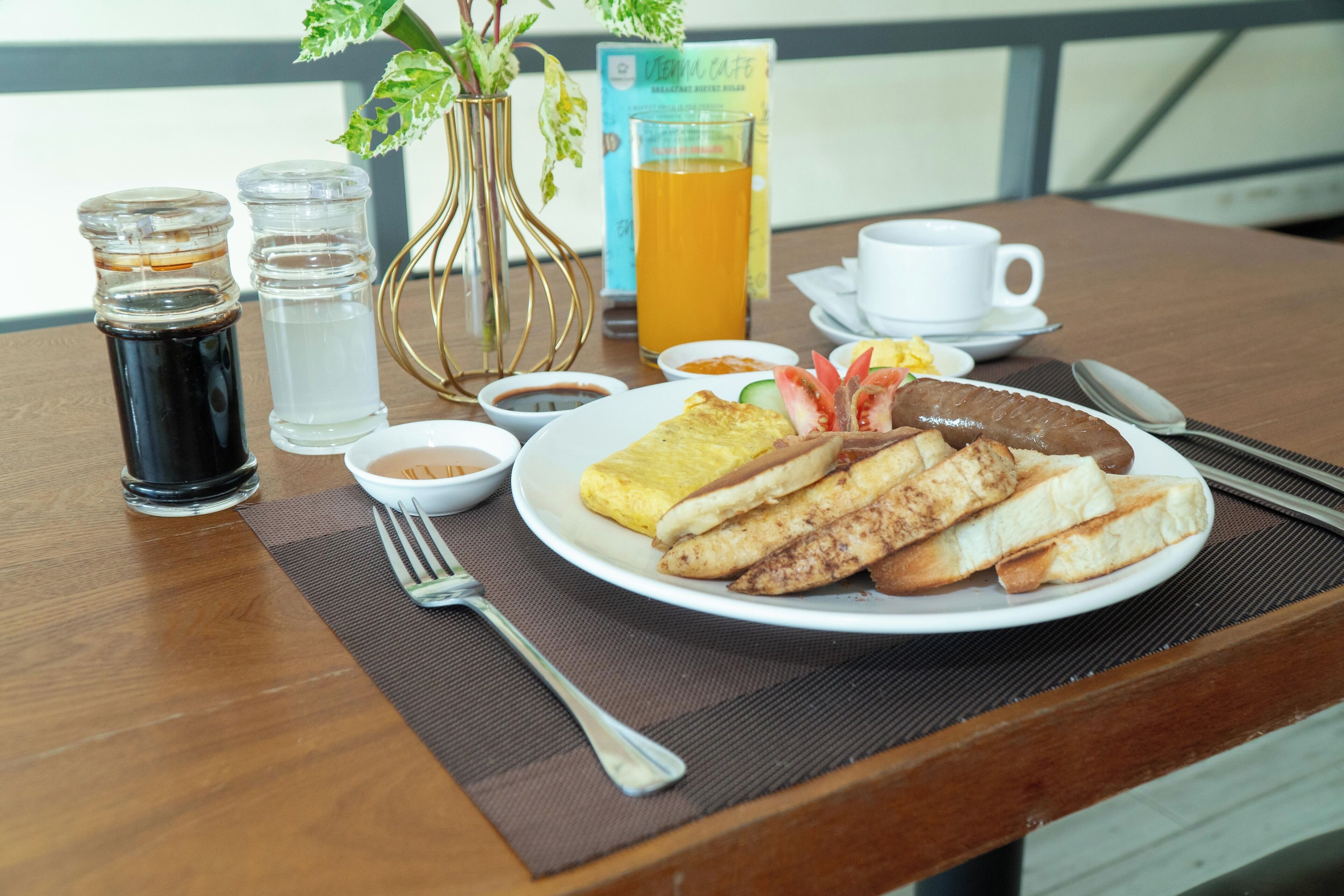 A breakfast setting with a plate of food, a glass of orange juice, and condiments on a wooden table.