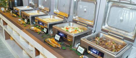 Un bufé con diversas estaciones de comida, incluyendo una estación de adobo de pollo y una estación de ensaladas.