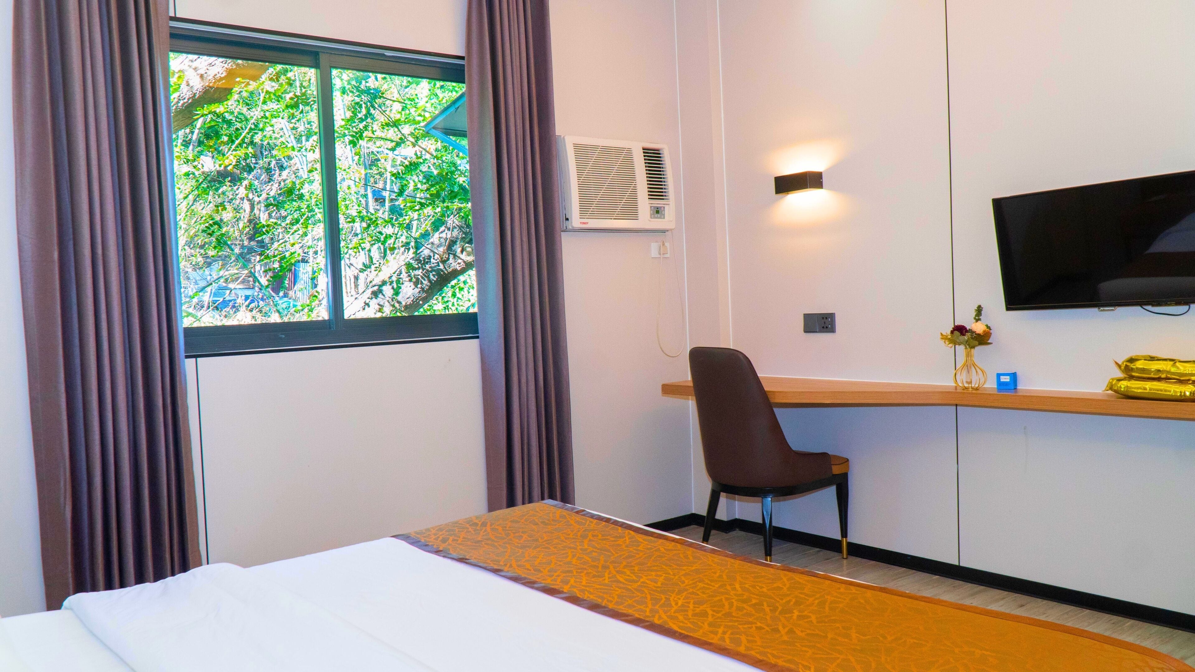 Habitación de hotel con cama, escritorio, silla, televisión y ventana con cortinas.