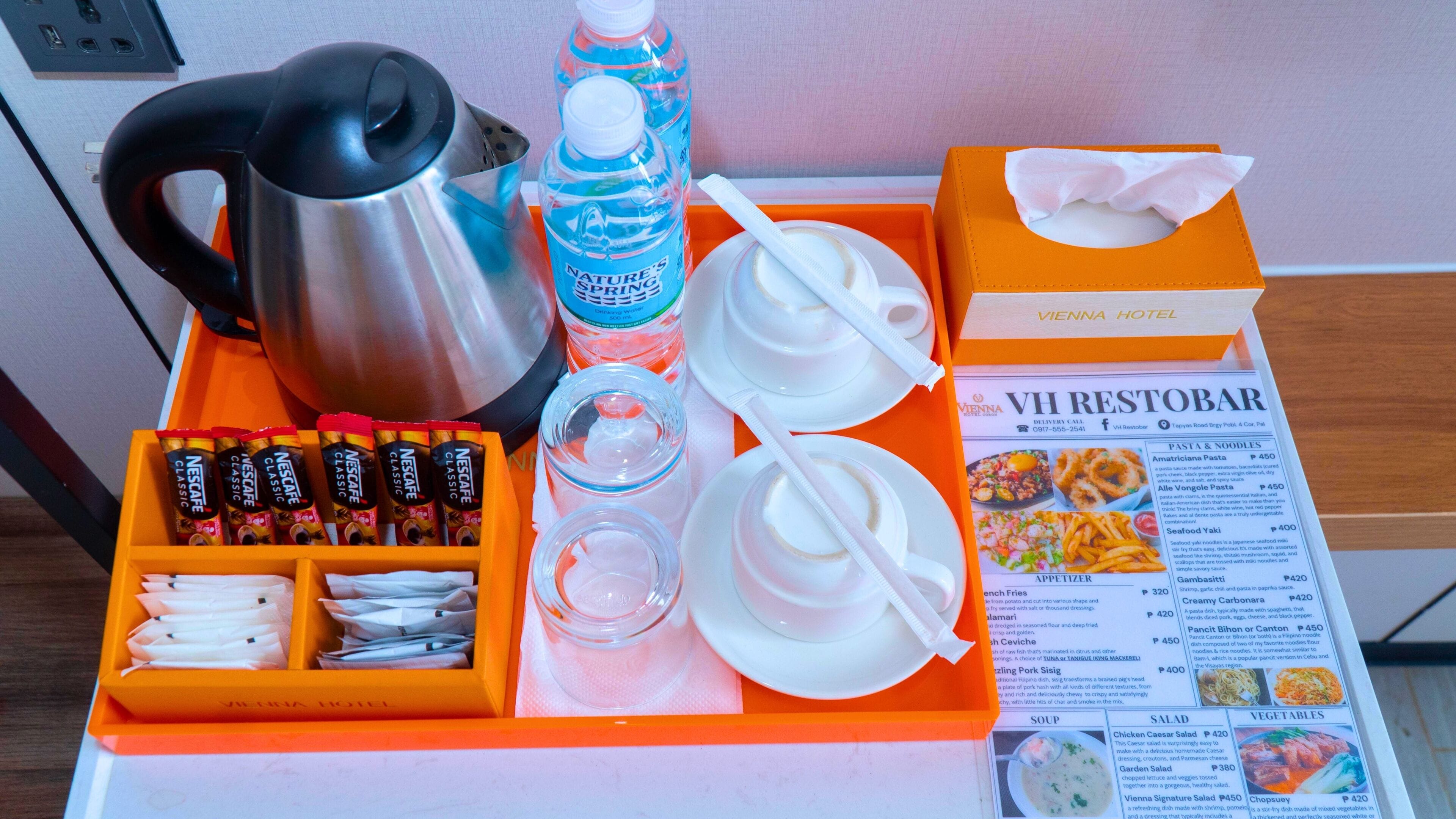 A hotel room's breakfast tray with a coffee maker, Nescafe Classic coffee packets, a water bottle, a glass, a napkin, and a menu.