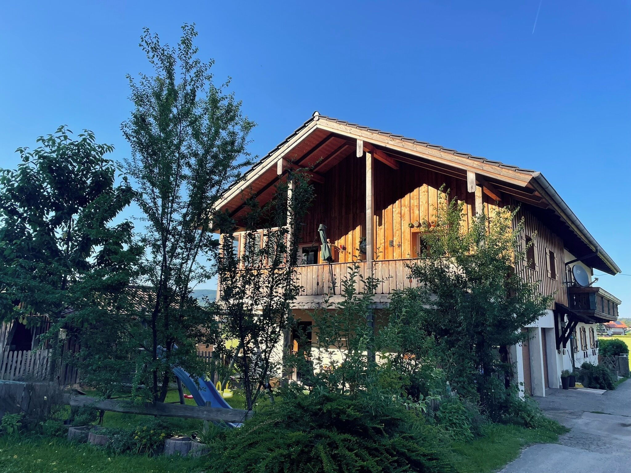Eine Holzhütte mit Balkon, umgeben von viel Grün und einem Spielplatz.