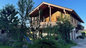 A wooden chalet with a balcony, surrounded by greenery and a playground. - Ferienwohnung Bergstation im Dopplerhof 2.OG 100qm, 2 Schlafzimmer (Piding)