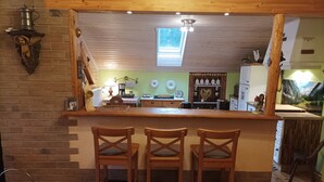 A kitchen with a wooden bar and three bar stools, a brick wall, and a window above the sink. - Ferienwohnung Bergstation im Dopplerhof 2.OG 100qm, 2 Schlafzimmer (Piding)