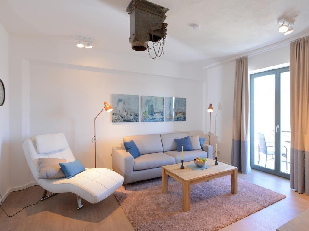 Un salon moderne avec un fauteuil blanc, un canapé, une table basse en bois et une grande fenêtre avec des rideaux.