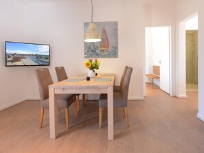 Un coin repas avec une table et des chaises en bois, un vase de fleurs, un tableau et un téléviseur accroché au mur.