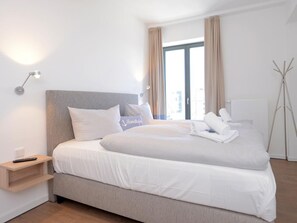 Une chambre d’hôtel moderne, dotée d’un grand lit, d’une table de chevet, d’une lampe et offrant une vue sur la ville par la fenêtre.