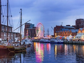 Ein Ufer mit einem großen Riesenrad, historischen Gebäuden und Booten, die am Wasser liegen.