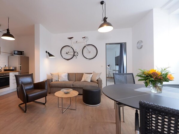 A modern living room with a sofa, a coffee table, a dining table, and a bicycle mounted on the wall.
